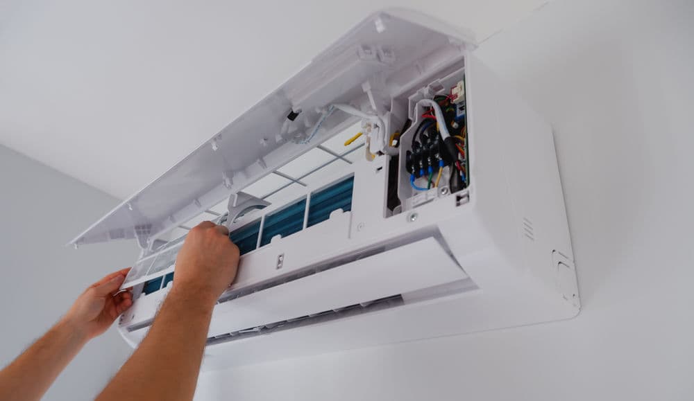 Person servicing a wall-mounted air conditioner unit, focusing on internal components.